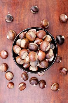 Fresh chestnuts in a bowl over a wooden background.