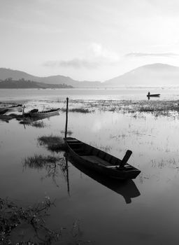 The quiet lake in early morning with black & white tone, fishermen make living on there, boat reflect on surface water