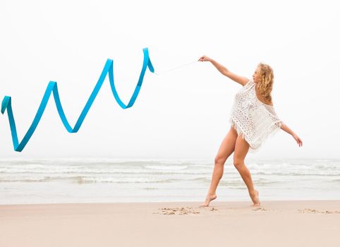 Young beautiful gymnast woman dance with ribbon on the beach at foggy day