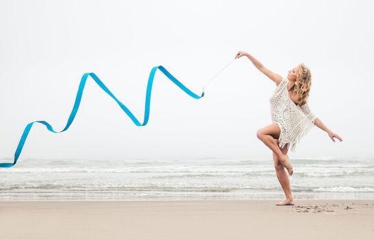 Young beautiful gymnast woman dance with ribbon on the beach at foggy day