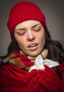 Sick Mixed Race Woman Wearing Winter Hat and Gloves Blowing Her Sore Nose with a Tissue.