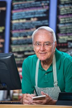 Senior man with apron behind counter taking orders
