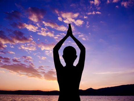 Silhouette of woman doing yoga meditation during sunset with natural golden sunlight at outdoor beach.