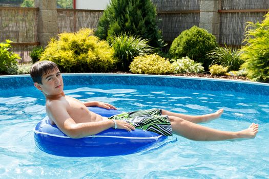 Teenage boy in the home swimming pool having fun and relax on a floating ring