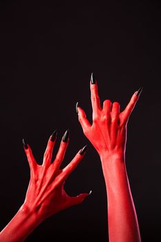 Red devil hands with long black nails, Halloween theme, studio shot on black background 