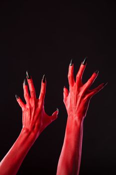 Red devil hands with sharp black nails, Halloween theme, studio shot on black background 