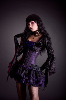 Beautiful witch in purple and black gothic Halloween outfit, studio shot on black background 