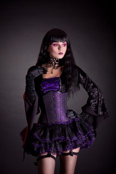 Romantic witch in purple and black gothic Halloween outfit, studio shot on black background 