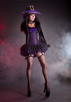 Pretty witch in purple and black gothic fantasy Halloween costume, full length shot  