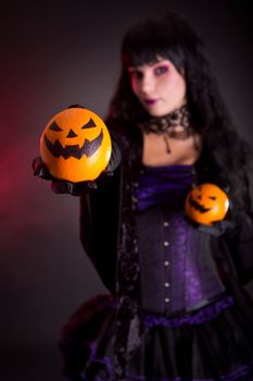 Beautiful witch holding Jack lantern oranges, selective focus on fruits 