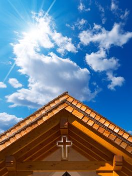 Small chapel with a wooden roof, cross and blue sky with clouds and sun rays
