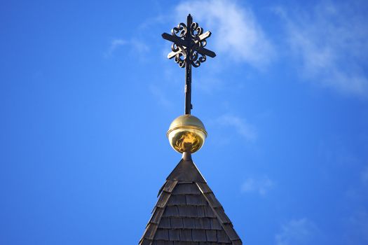 Wooden roof of church with wrought iron cross against the blue sky