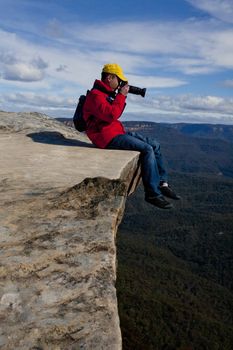 Tourist or photographer on a cliff edge taking photos  of a mountainous landscape