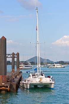Yacht at berth in background of ships and blue sky, Thailand.