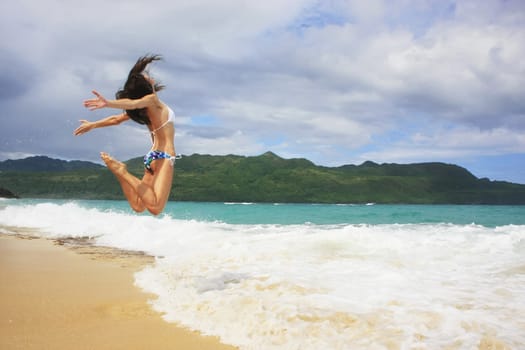 Young woman in bikini jumping at Rincon beach, Samana peninsula, Dominican Republic