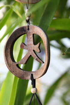 Handcrafted rustic wooden ornament with a circular frame enclosing an ethnic symbol hanging outdoors with two thongs attached by beads