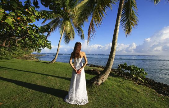 Young woman in wedding dress standing by palm tree