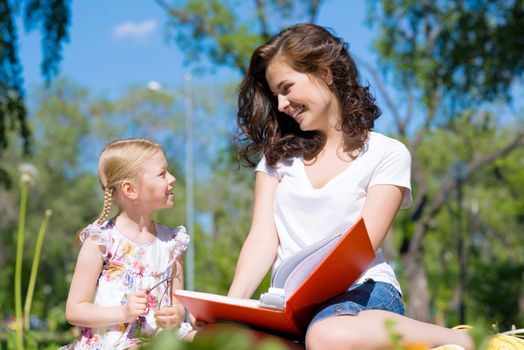 girl with the teacher reading a book together in the summer park