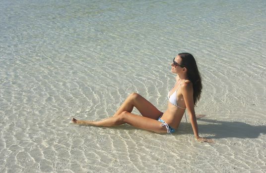 Young woman in bikini sitting in clear shallow water