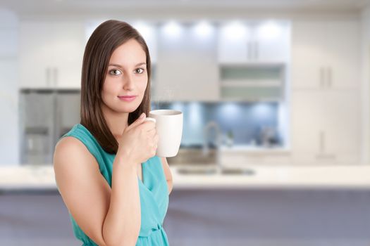 Young woman drinking a hot tea from a white cup in a kitchen