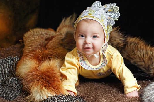 Blue-eyed baby lying on fur litter near the hauberk, fox pelt in the background