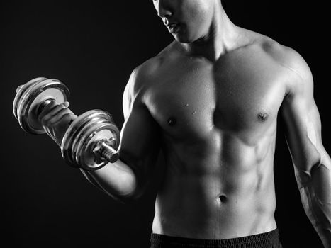 Photo of an Asian male exercising with a dumbbell and doing bicep curls over dark background.