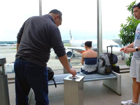 Airline passenger stubbing out a cigarette in a smoking room before a flight.