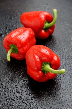 Three red bell peppers on black table after rain