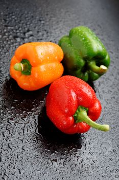Orange, red and green bell peppers on black table after rain