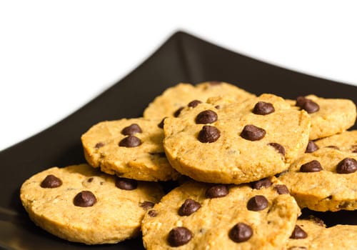 Closeup of chocolate chip cookies on a square black plate, isolated on white background