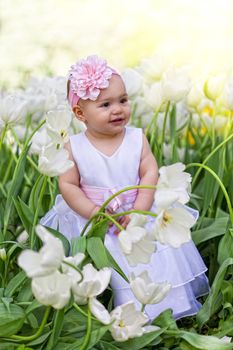 Little girl in an elegant dress to stand near blossoming tulips