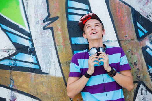 Close-up portrait of happy teens boy with headphones near painted wall listening to music
