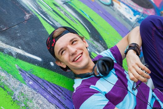Close-up portrait of happy teens boy with headphones near painted wall listening to music
