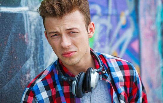 Close-up portrait of happy teens boy with headphones near painted wall