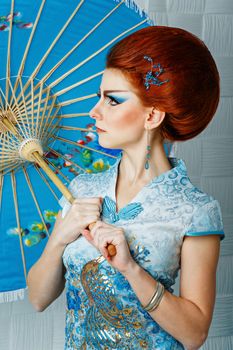 Attractive geisha in a smart dress with an umbrella, photographed in the studio