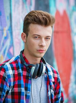 Close-up portrait of happy teens boy with headphones near painted wall. Vertical view