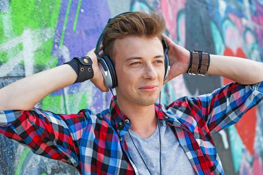 Close-up portrait of happy teens boy with headphones near painted wall listening to music