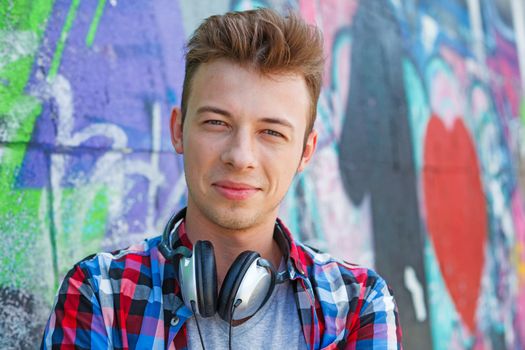 Close-up portrait of happy teens boy with headphones near painted wall listening to music