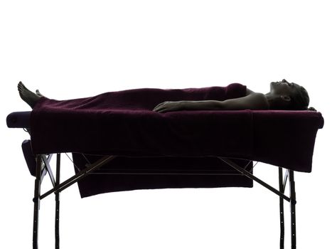 one woman lying on a massage table in silhouette studio on white background