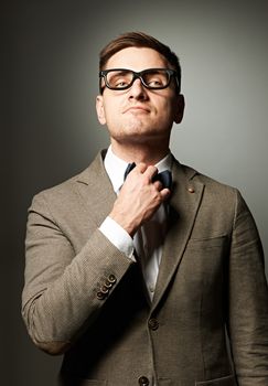 Confident nerd in eyeglasses adjusting his bow-tie against grey background