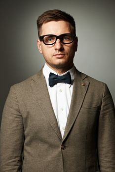 Confident nerd in eyeglasses and bow tie against grey background