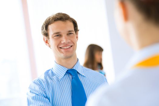 young businessman holds up a pen, talking with a colleague in front of