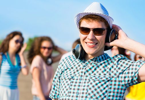 young man in sunglasses, headphones holds a hand on a background of blue sky and friends