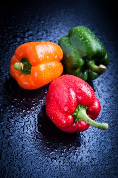 Orange, red and green bell peppers on blue table after rain