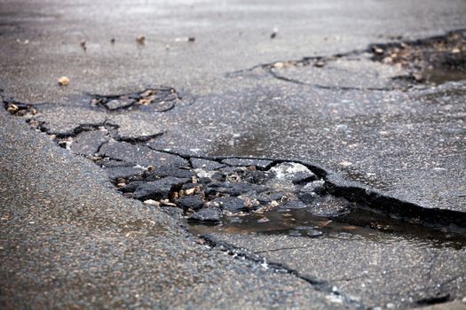 Damaged asphalt pavement road with potholes caused by freeze and thaw cycle during winter.