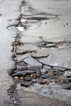 Damaged asphalt pavement road with potholes caused by freeze and thaw cycle during winter.