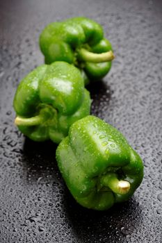 Three green bell peppers on black table after rain