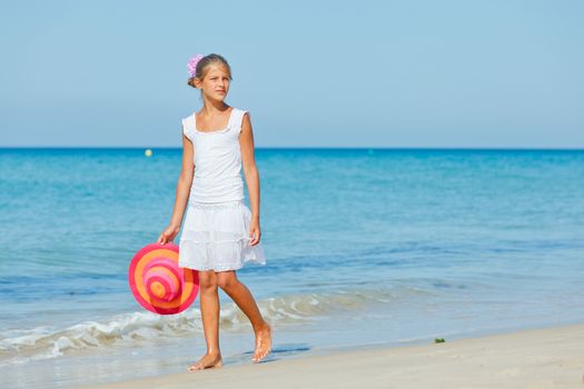 Relaxing beach girl walking with a sun hat at the beach.
