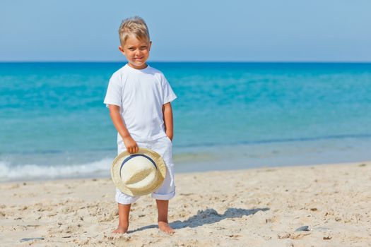 Smiling cute boy with a sun hat at the tropical beach.