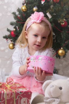 Cute girl in pink under Christmas tree with giftbox